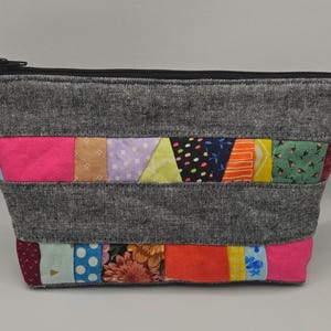 May include: A gray denim zippered pouch with a patchwork design. The patchwork is made of colorful fabric scraps in various patterns and colors, including pink, blue, green, yellow, and orange.