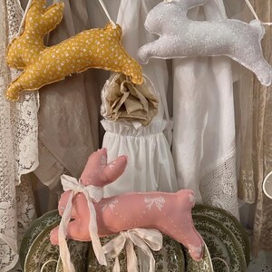 May include: A white wire dish rack with green and white patterned plates. A pink bunny, a yellow bunny, and a white bunny are hanging on the wall behind the dish rack.