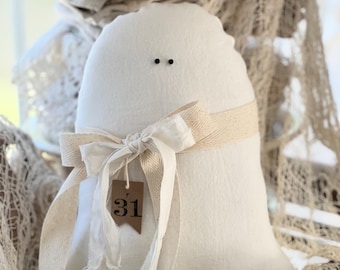Puede incluir: Fantasma de fieltro blanco con ojos negros y una cinta marrón atada alrededor del cuello. El fantasma tiene una etiqueta marrón con el número 31.