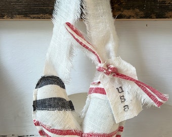 May include: A white heart-shaped pillow with red and black stripes, hanging from a wooden hook. The pillow has a frayed edge and a tag that says "D & C".