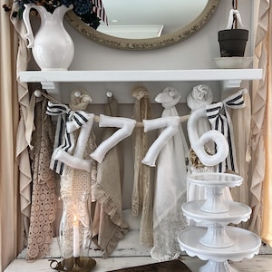 May include: A decorative display featuring American flags, a white pitcher with floral accents, and the number "1776" crafted from fabric. The display includes a tiered cake stand and a vintage-style wooden cutting board, evoking a patriotic theme.