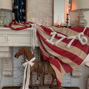 May include: A patriotic display featuring a vintage American flag draped over a white mantel. A wooden horse with a saddle and white ribbon stands in front of the mantel. The Declaration of Independence is framed above the mantel.