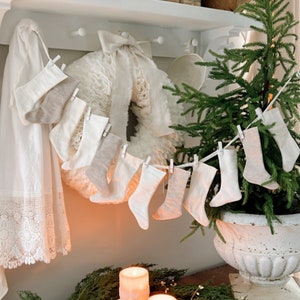 May include: A white shelf with a white teapot, a white wreath, and a string of small white stockings hanging from it. A small green Christmas tree is in a white planter on a wooden table with a green wreath and three white candles.