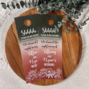 May include: Two black and green door hangers with a white floral design and a gradient background that fades from pink to red. The text on the door hangers reads "Shhh... Please do not disturb! We danced the night away at Tiffany and Ryan's Wedding!"