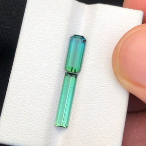 May include: Two green and blue rectangular gemstones on a white background. The gemstones are cut into a rectangular shape with facets.