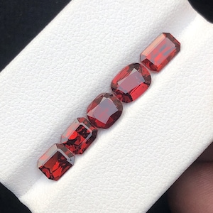 May include: Five red gemstone cabochons in a rectangular shape, arranged in a row on a white surface.