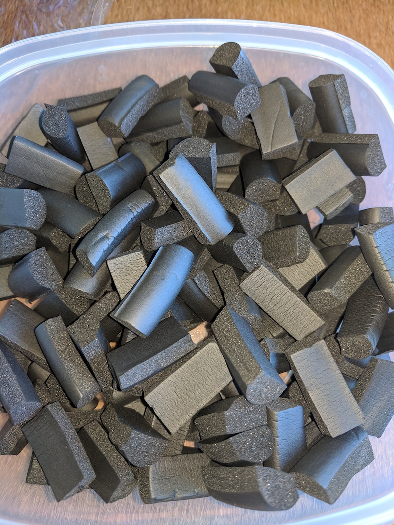 K&ouml;nnte beinhalten: Ein Beh&auml;lter gef&uuml;llt mit schwarzen Schaumgummi-St&uuml;cken in verschiedenen Formen und Gr&ouml;&szlig;en. Die St&uuml;cke sind alle auf eine &auml;hnliche L&auml;nge geschnitten und haben eine leicht abgerundete Kante.