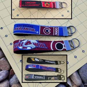 May include: A collection of fabric keychains featuring various sports team logos. The keychains display the logos and team names of the Chicago Blackhawks, Colorado Avalanche, Pittsburgh Penguins, New York Rangers, and Vegas Golden Knights.