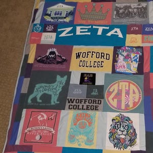 May include: A patchwork quilt constructed from various Zeta Tau Alpha sorority t-shirts. The design features multiple graphic prints, including a crown, a lion, Wofford College text, and various ZTA logos in diverse colors like pink, blue, and yellow.