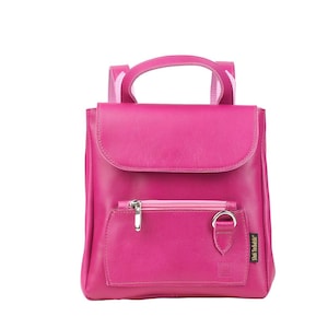 Könnte beinhalten: Ein kleiner rosa Lederrucksack mit einer Fronttasche und einem silbernen Reißverschluss. Der Rucksack hat ein kleines silbernes Schild mit dem Text "Stan & Ollie" darauf.