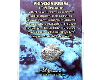 May include: A silver coin from the Princess Louisa shipwreck of 1743, displayed in a clear case. The coin is from the English East Indiaman, which sank near the Cape Verde Islands. The text on the case describes the coin's history.
