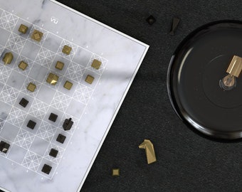 May include: A marble chessboard with gold and black chess pieces. The board is set up for a game of chess. The pieces are arranged in a strategic pattern. The board is on a black surface. There are also some extra pieces on the surface.