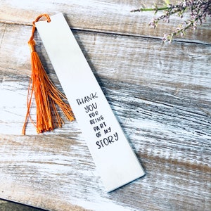 May include: A white metal bookmark with a tassel. The bookmark has the text "Thank you for being part of my story" engraved on it.