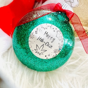 May include: Green glitter Christmas ornament with a white circle sticker that says "Happy Holi-Daze" with a marijuana leaf design.
