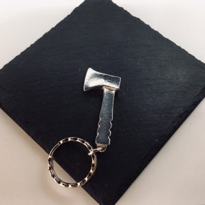 May include: Silver axe keychain with a textured handle and a silver key ring.