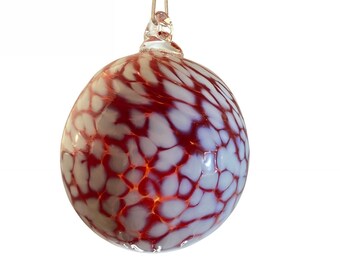 May include: Red and white glass Christmas ornament with a swirling pattern. The ornament is hanging from a silver string.