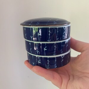 May include: A blue and white ceramic stacking storage container with a lid. The container has a floral design.