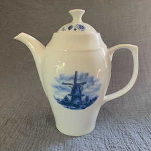 Puede incluir: Tetera de porcelana blanca con un diseño de molino de viento azul y blanco. La tetera tiene una tapa y un asa.