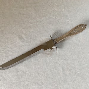 May include: A silver knife with a serrated blade and an ornate handle. The knife is designed for cutting bread.