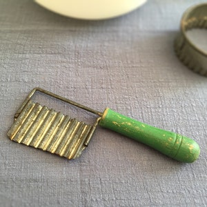 May include: A vintage green-handled metal kitchen tool with a wavy blade for cutting food.