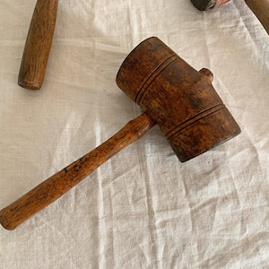 May include: A wooden mallet with a brown handle and a round head. The head has a grooved design.