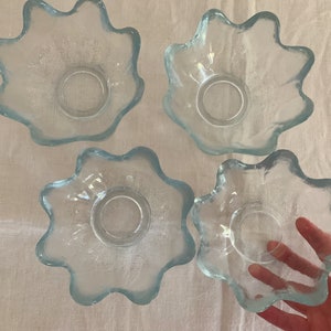 May include: Four clear glass bowls with a wavy, scalloped edge. The bowls are arranged in a square pattern on a white surface.