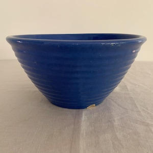 May include: A blue ceramic bowl with a ribbed exterior. The bowl has a wide, open top and a rounded base. The bowl is a solid, vibrant blue color and appears to be handmade.