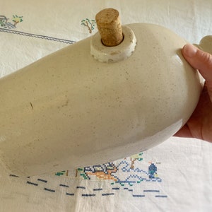 May include: A white ceramic bottle with a cork stopper. The bottle has a speckled glaze and is marked with the text "ESTD 1874" and "ENGLAND".