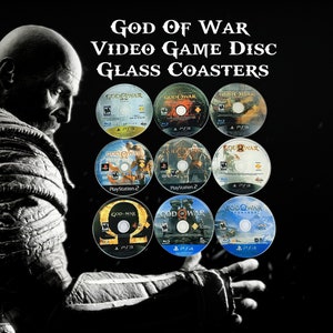 May include: Nine glass coasters featuring the "God of War" video game disc designs. The coasters display various game covers, including PlayStation 2 and PS3 versions. Text on the coasters reads "God of War" and game platform names.