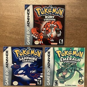 May include: Three Game Boy Advance video game cartridges: Pokémon Ruby Version, Pokémon Sapphire Version, and Pokémon Emerald Version. Each cartridge features a different Pokémon character on the cover, with the game title prominently displayed.