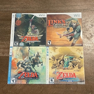 May include: Four Nintendo Wii game cases featuring The Legend of Zelda series. The cases display colorful artwork of characters and scenes from the games, including Link with a sword and bow. Titles include "Skyward Sword", "Link's Crossbow Training", "Twilight Princess HD", and "Wind Waker HD".