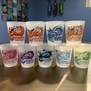May include: A set of nine frosted glass shot glasses, each featuring a colorful illustration of a different creature and a unique phrase. The phrases include Ignite the Flame, Evoke the Base, Surge the Tide, Strike the Bolt, Heart the Charm, Focus the Mind, Chase the Night, Chill the Veins, and Embrace the Nature.