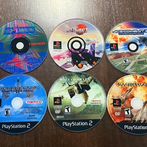 May include: Six PlayStation 2 video game discs featuring the "Ace Combat" series. The discs have colorful graphics with images of fighter jets and the game titles. The games include "Ace Combat," "Ace Combat 2," "Ace Combat 3," "Ace Combat 4," "Ace Combat 5," and "Ace Combat Zero."
