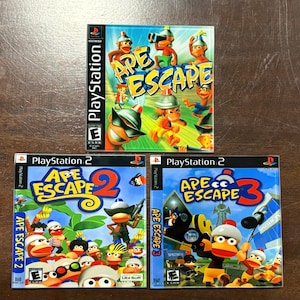 May include: Three PlayStation video game cases are displayed. The top case is for "Ape Escape" for PlayStation, and the bottom two are "Ape Escape 2" and "Ape Escape 3" for PlayStation 2. The game covers feature cartoon monkeys.