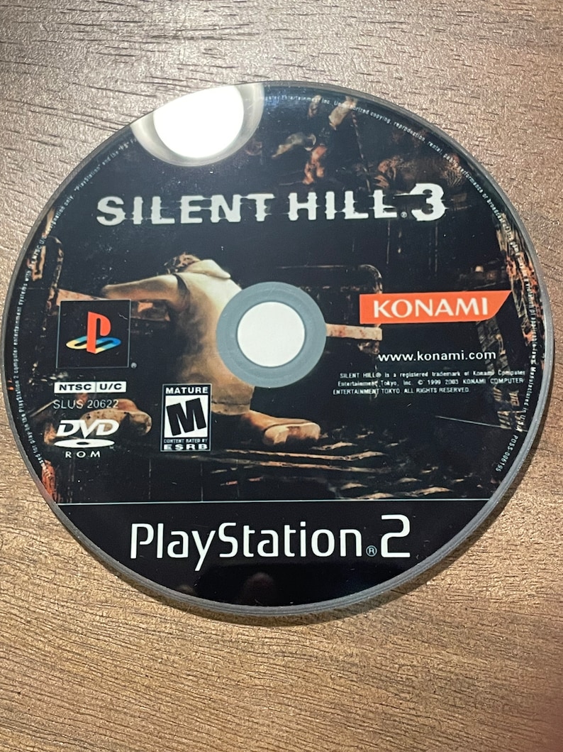 May include: A black PlayStation 2 DVD game disc for Silent Hill 3. The disc has white text and a graphic of a figure. The game title and the PlayStation 2 logo are visible. The disc also features the Konami logo.