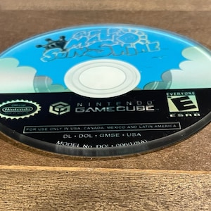 May include: A Nintendo GameCube disc with the game title "Super Mario Sunshine" in blue and white. The disc has a black border with the Nintendo GameCube logo and ESRB rating. The disc is for use only in USA, Canada, Mexico, and Latin America.