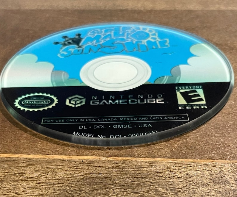May include: A Nintendo GameCube disc with the game title "Super Mario Sunshine" in blue and white. The disc has a black border with the Nintendo GameCube logo and ESRB rating. The disc is for use only in USA, Canada, Mexico, and Latin America.
