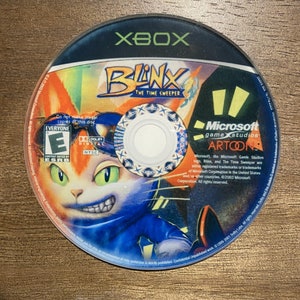 May include: A circular Xbox game disc for "Blink: The Time Sweeper." The disc features a colourful illustration of a cat-like character with green eyes and a blue outfit. The disc also displays the Xbox logo, ESRB rating, and Microsoft Game Studios branding.
