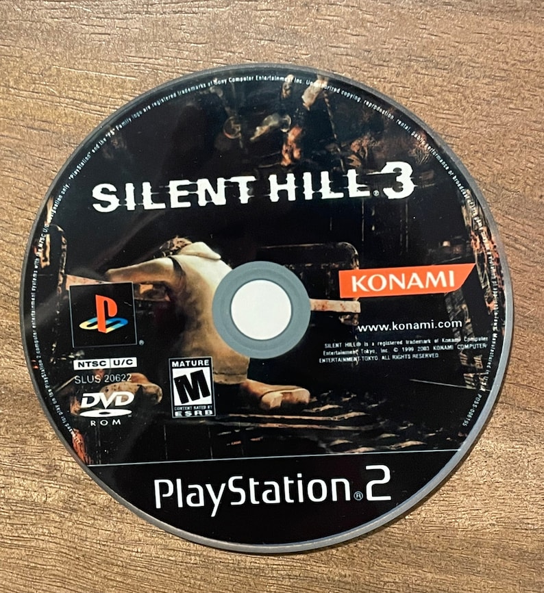 May include: A black DVD-ROM disc for the PlayStation 2 console. The disc features the game title "SILENT HILL 3" in white lettering, the Konami logo, and the PlayStation 2 logo. The disc is rated "M" for Mature.