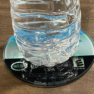 May include: A clear plastic water bottle on a GameCube disc. The disc is black with blue and white details, and features the Nintendo GameCube logo and ESRB rating. The bottle contains clear water.