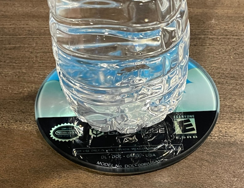 May include: A clear plastic water bottle on a GameCube disc. The disc is black with blue and white details, and features the Nintendo GameCube logo and ESRB rating. The bottle contains clear water.