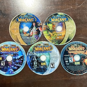 May include: Five World of Warcraft game DVDs are displayed, each with a unique design. The discs feature the game's logo and various character illustrations in vibrant colors. The game titles include "Wrath of the Lich King" and "Cataclysm".