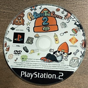 May include: A PlayStation 2 game disc for Parappa the Rapper 2. The disc features cartoon graphics, including the game's title, a character in an orange beanie, and the PlayStation logo. The disc is PAL format.