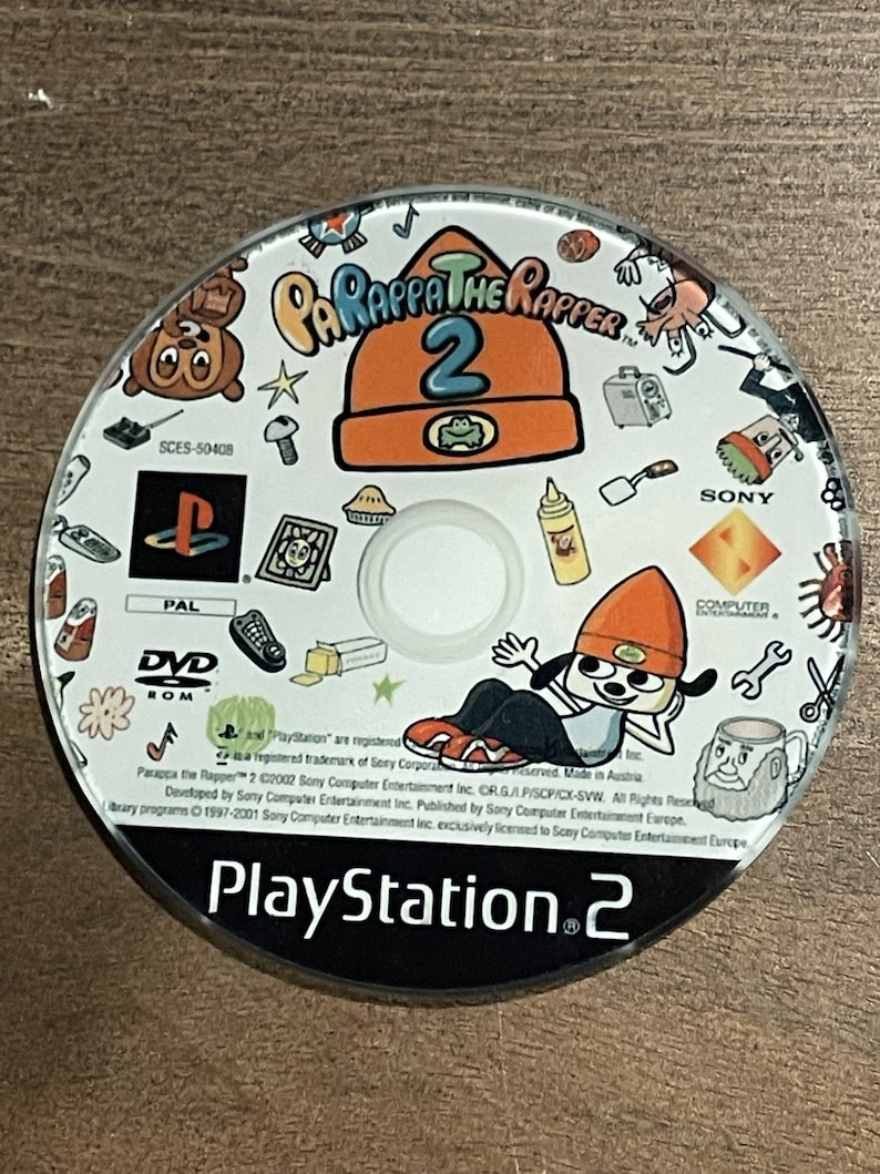 May include: A PlayStation 2 game disc for Parappa the Rapper 2. The disc features cartoon graphics, including the game's title, a character in an orange beanie, and the PlayStation logo. The disc is PAL format.