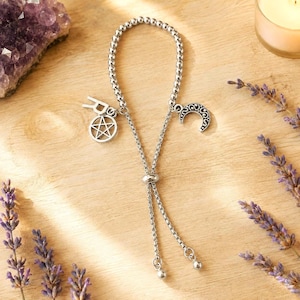 May include: A silver-toned adjustable bracelet featuring a small letter R charm, a pentagram charm, and a crescent moon charm. The bracelet is constructed with a delicate beaded chain and a sliding bead mechanism for size adjustment.
