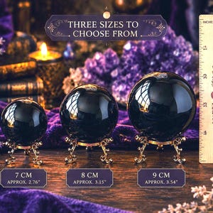 May include: Three polished black spheres on ornate gold-toned metal stands. A wooden ruler shows sizes of 7 cm, 8 cm, and 9 cm. Text reads: THREE SIZES TO CHOOSE FROM, 7 CM, 8 CM, and 9 CM. The spheres are arranged in a row from smallest to largest.