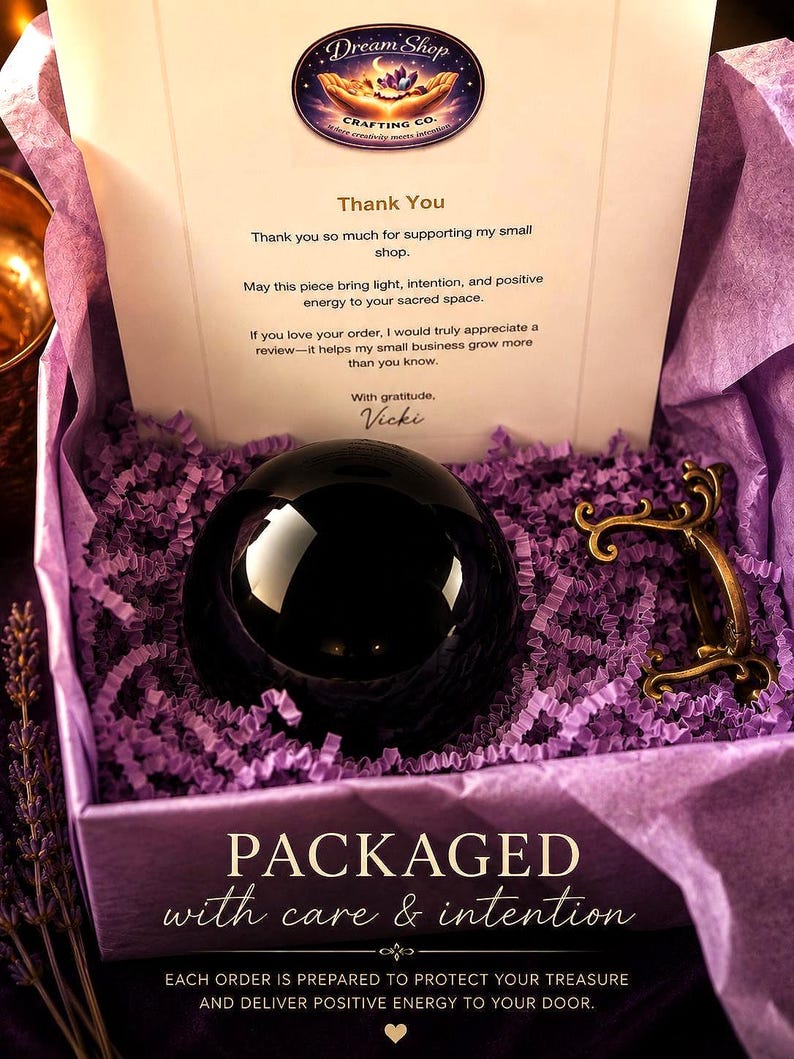 May include: A black polished sphere sits in a purple paper-filled box alongside a small ornate gold-toned metal stand. A thank you note from Dream Shop Crafting Co. is included, with text stating: PACKAGED with care & intention. EACH ORDER IS PREPARED.