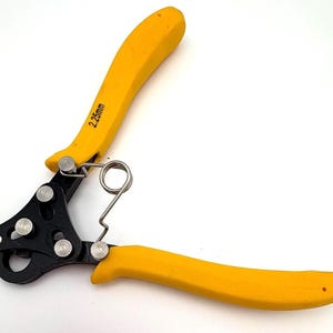 Puede incluir: Pelacables amarillo y negro con un resorte y el texto "2.25mm" impreso en el mango amarillo. La herramienta tiene una cabeza negra con remaches plateados y mangos amarillos.