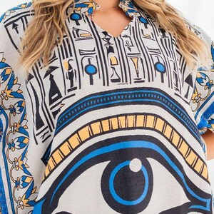 May include: A cream-colored tunic with a large blue eye design and hieroglyphic patterns. The tunic has a V-neck and blue fringe detailing. The text "KEHOT" and "Every thread holds quality" are visible at the top.