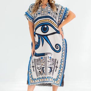 May include: A white, knee-length caftan dress with a blue and gold Eye of Horus design. The dress has short sleeves and a split hem with blue fringe. The text "Every thread holds quality" is at the top left.